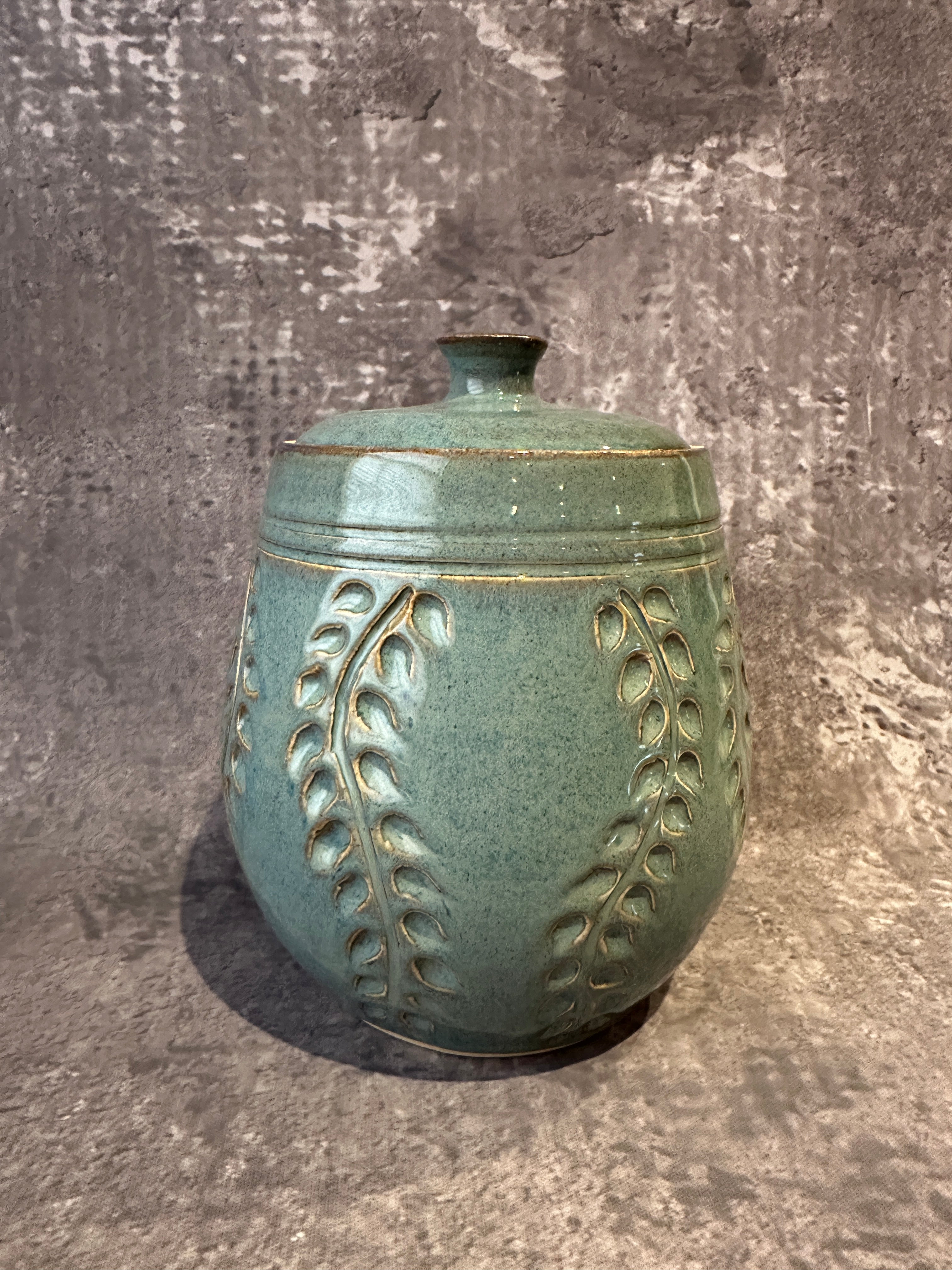 Handcrafted  blue ceramic lidded canister with carved leaf patterns on surface.