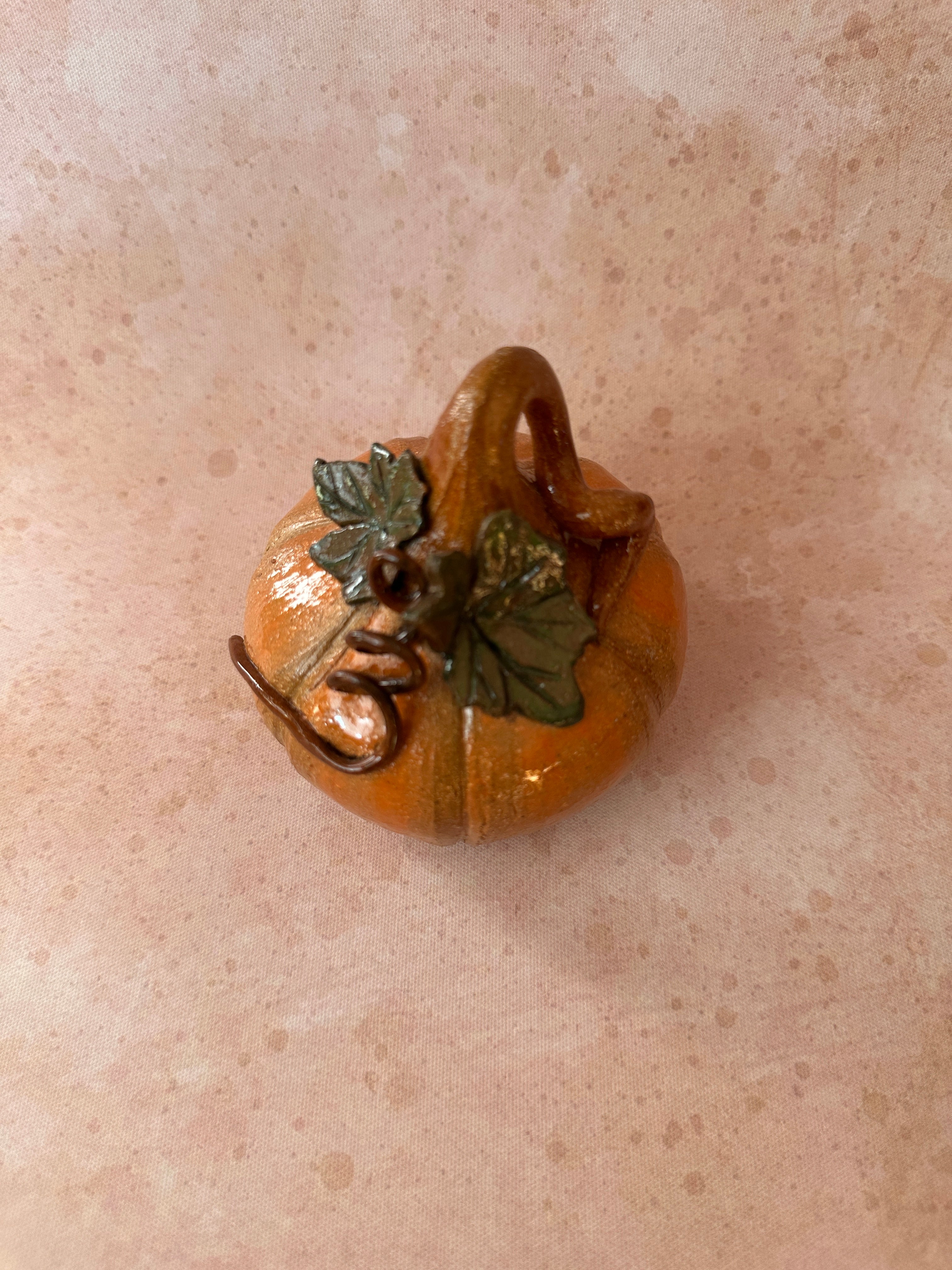 Decorative pumpkin with leaves on a rustic orange surface.
