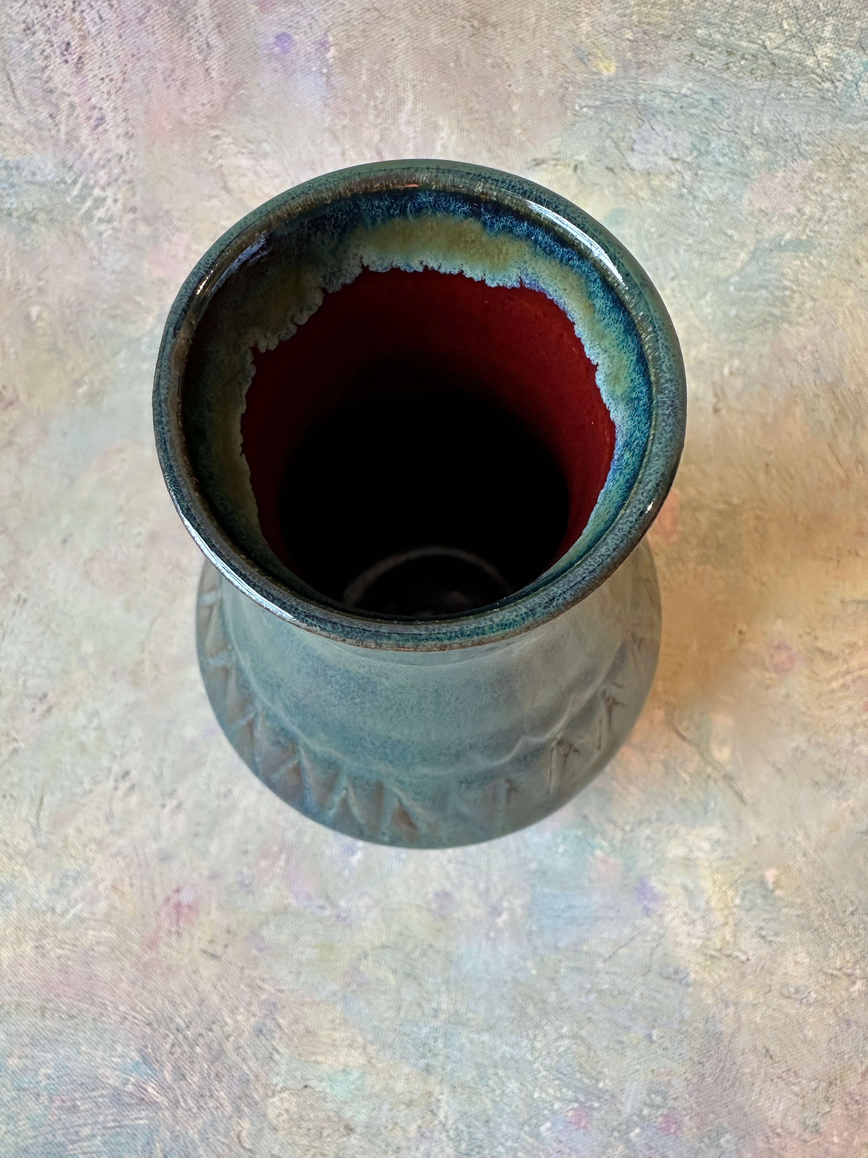 A handmade ceramic vase with a glossy dark green and copper glaze, with the inside finished in a rich red glaze. The carved texture surface adds depth and changes colors in different lighting.