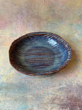 A handcrafted stoneware bowl with a textured, ribbed interior and a glossy, denim blue glazed interior, shown from a top-down view.