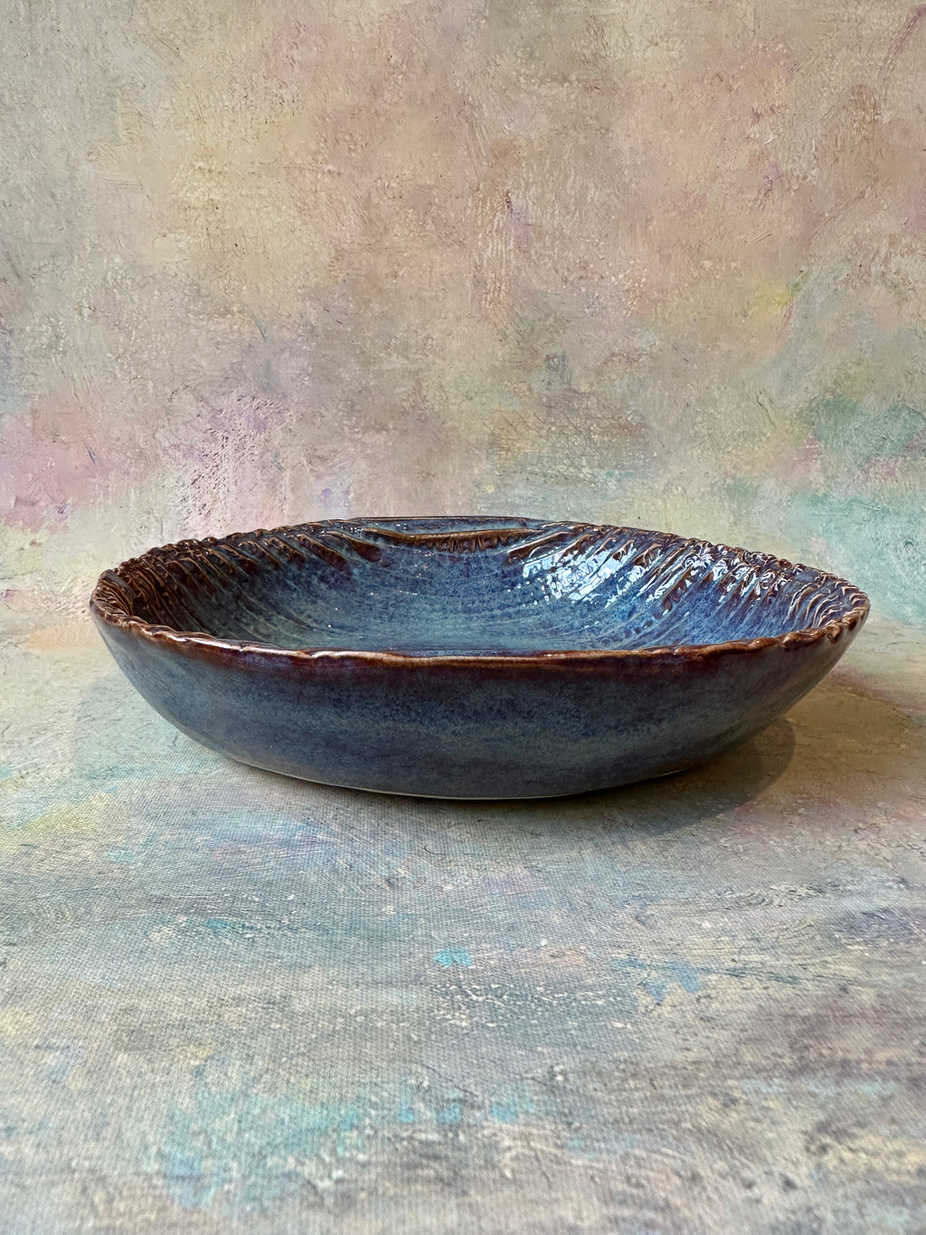 A handmade ceramic bowl with a textured, ribbed surface and a glossy dark denim blue glaze that breaks a beautiful red brown on the texture.