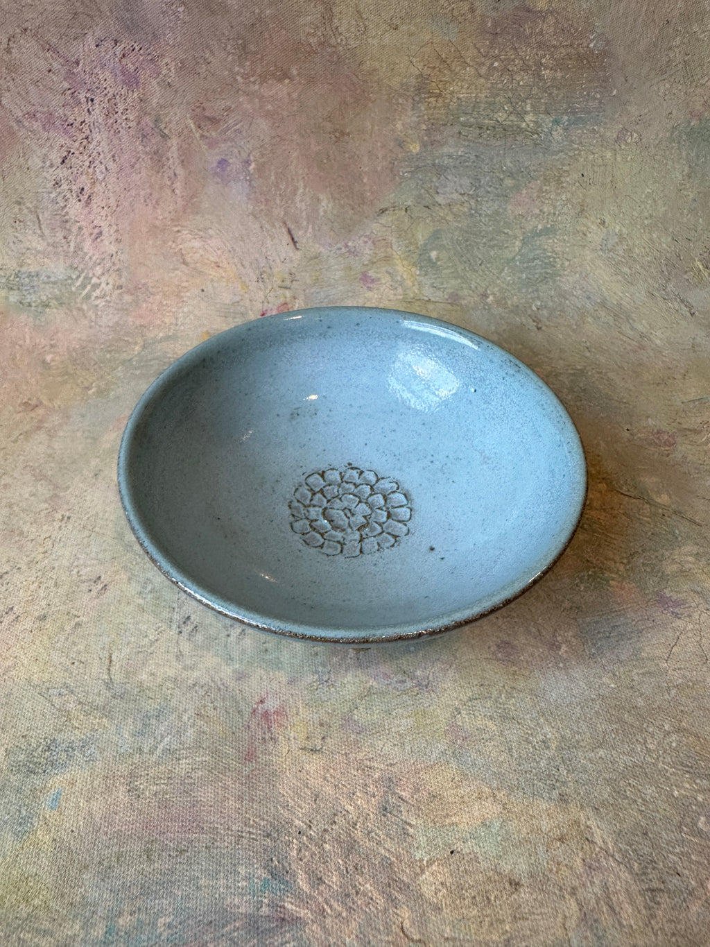 A handmade ceramic garlic grater bread dipping oil bowl with a light robins egg blue glaze and a textured floral center for garlic grating.